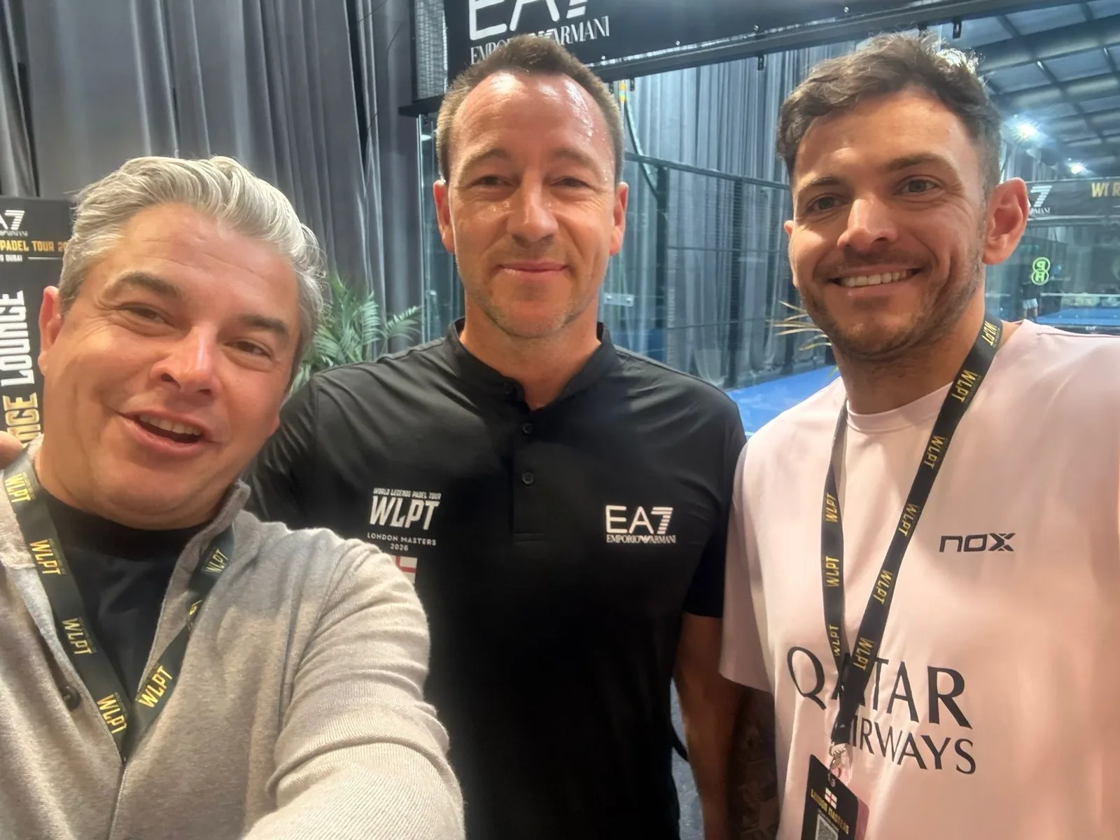 John Terry in his black WLPT London Masters polo with two of the PadX and Genius Digital Labs team, the floodlit padel courts behind them.